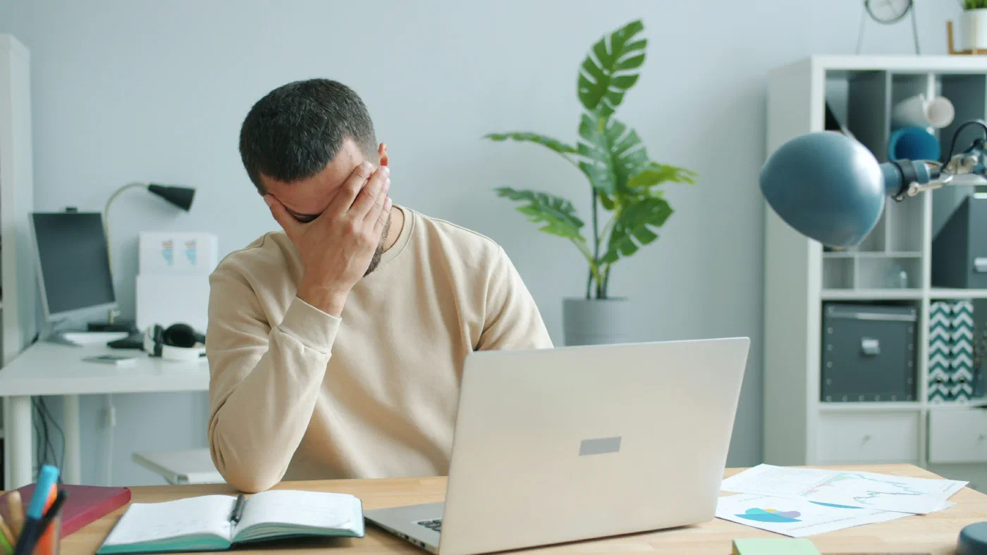 A man rubbing his face in front of a laptop