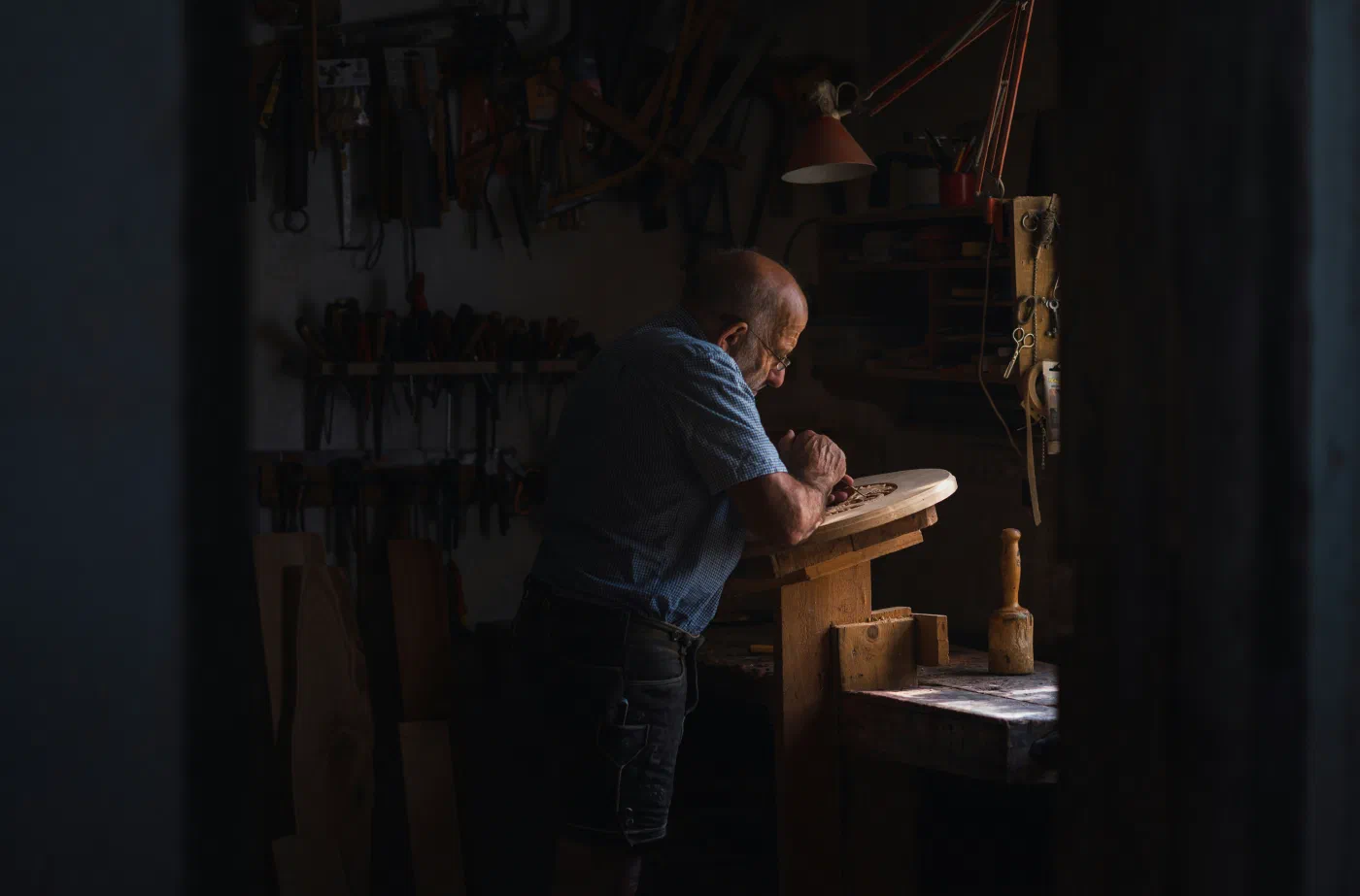 An elderly craftsman carving a wooden piece at his workbench